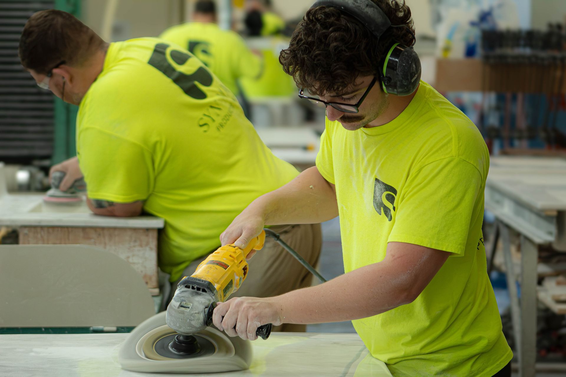 Workers in neon yellow shirts sanding a tabletop in a workshop