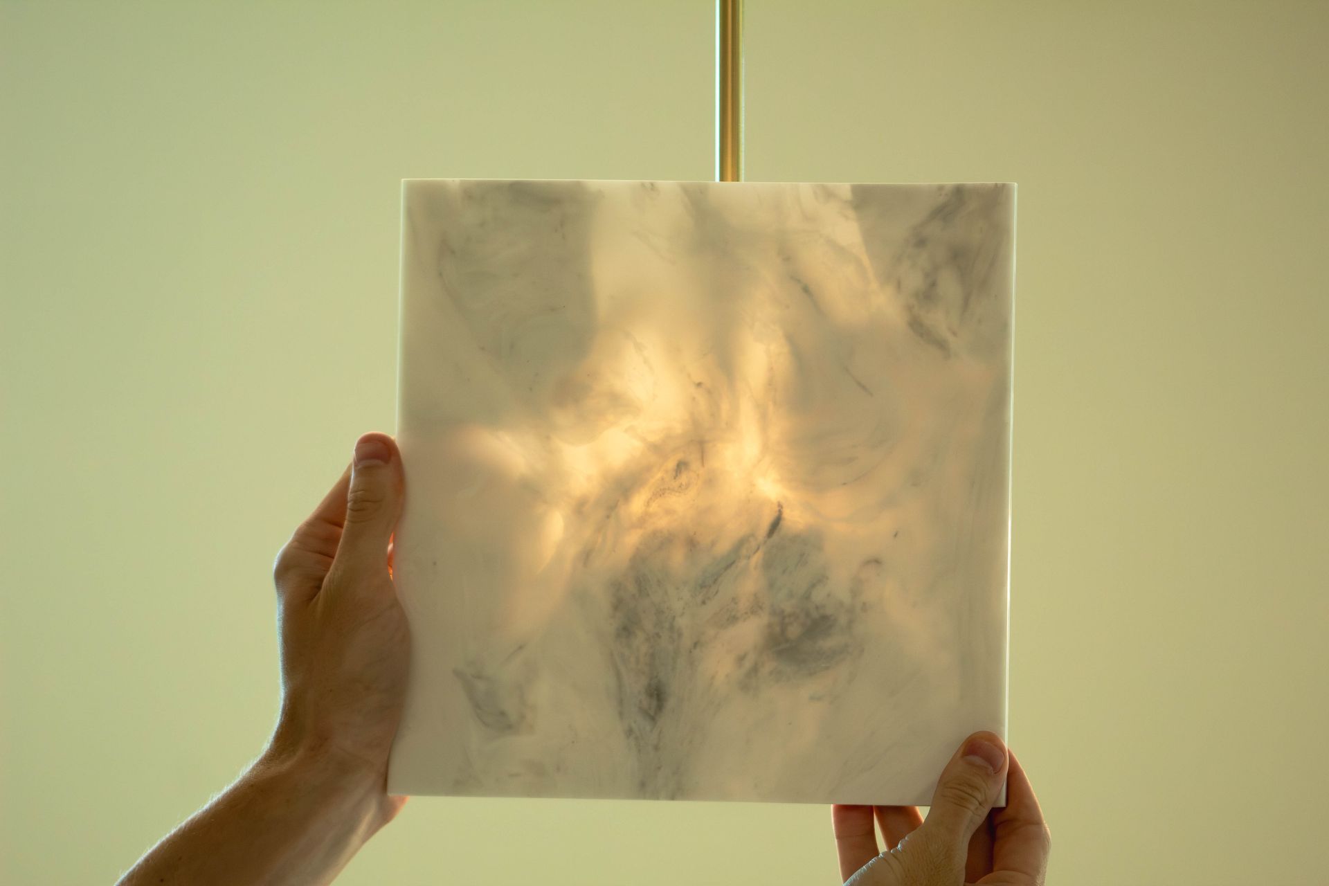 Hands hold a translucent square sheet glowing with warm light against a pale background