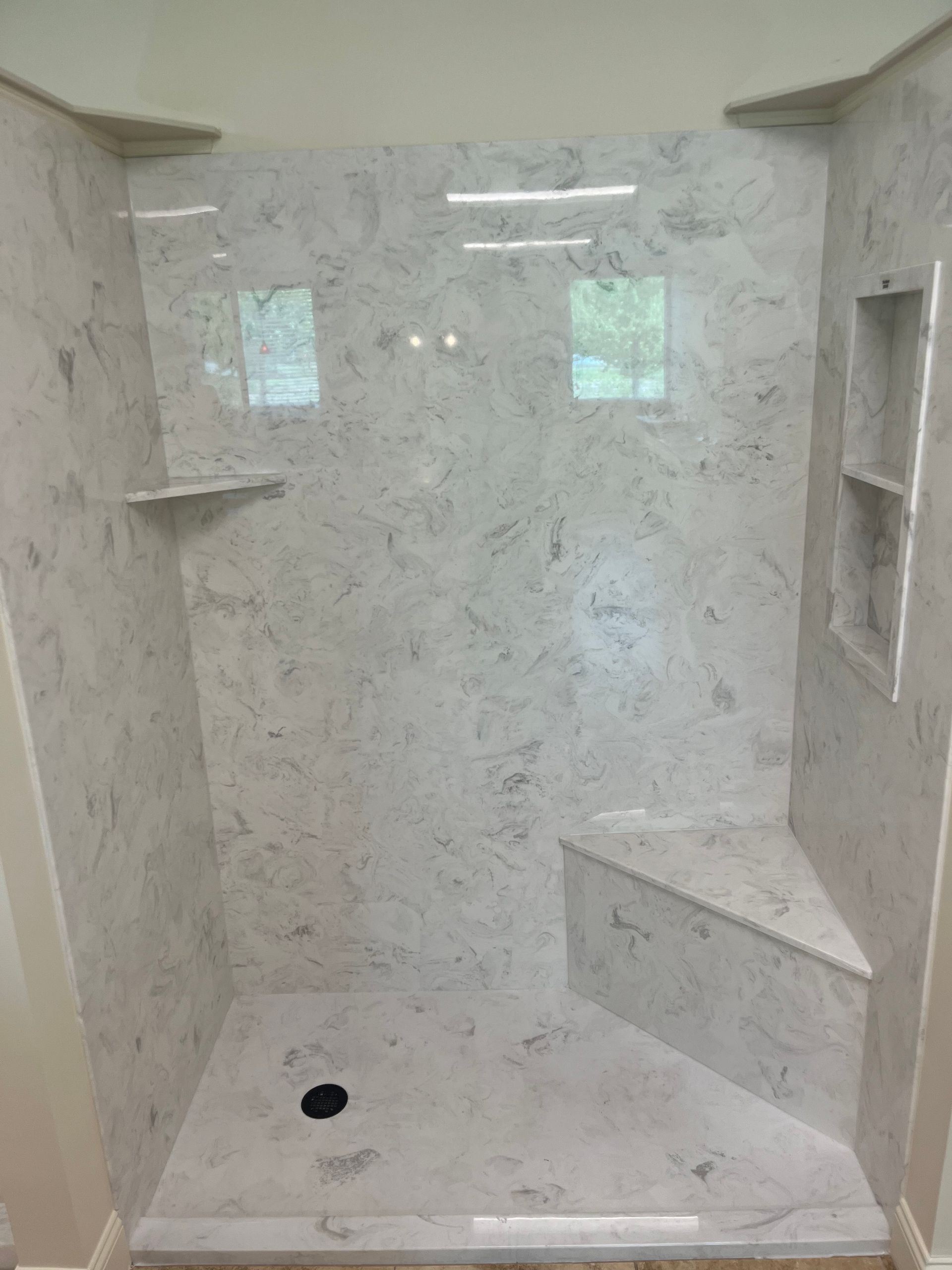 Walk-in shower with white marble tile, built-in shelves, bench, and a drain on the floor
