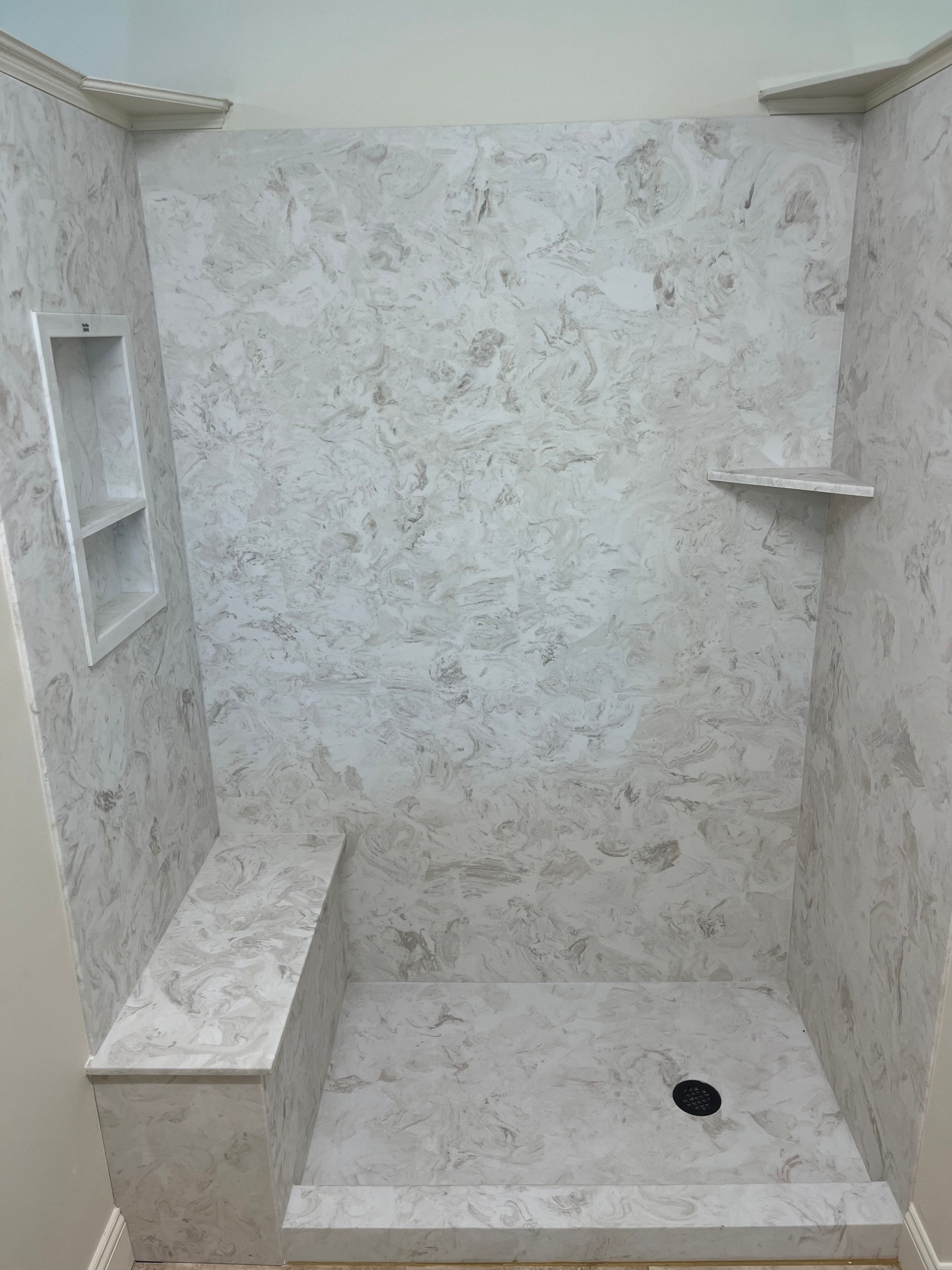 Empty tiled shower stall with built-in shelves and a small step-in ledge