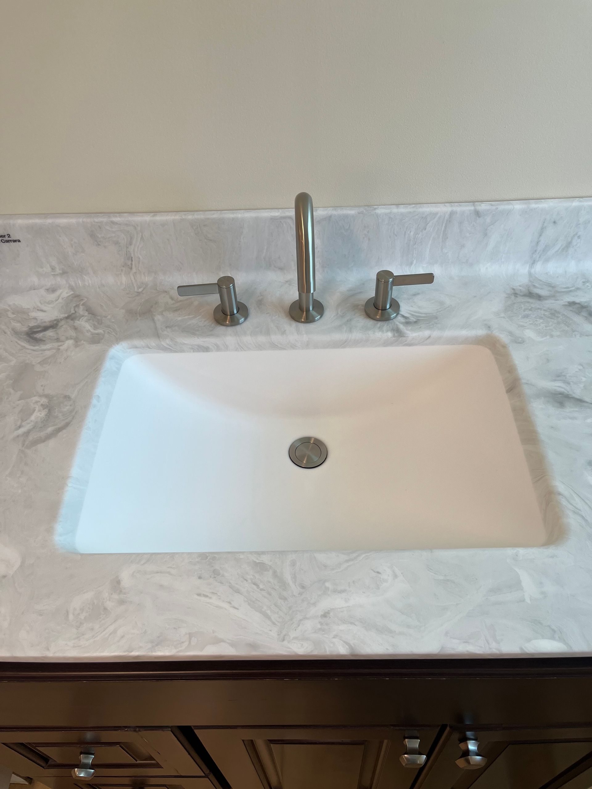 White bathroom sink with chrome faucet and handles on a marble countertop, with wooden cabinets below
