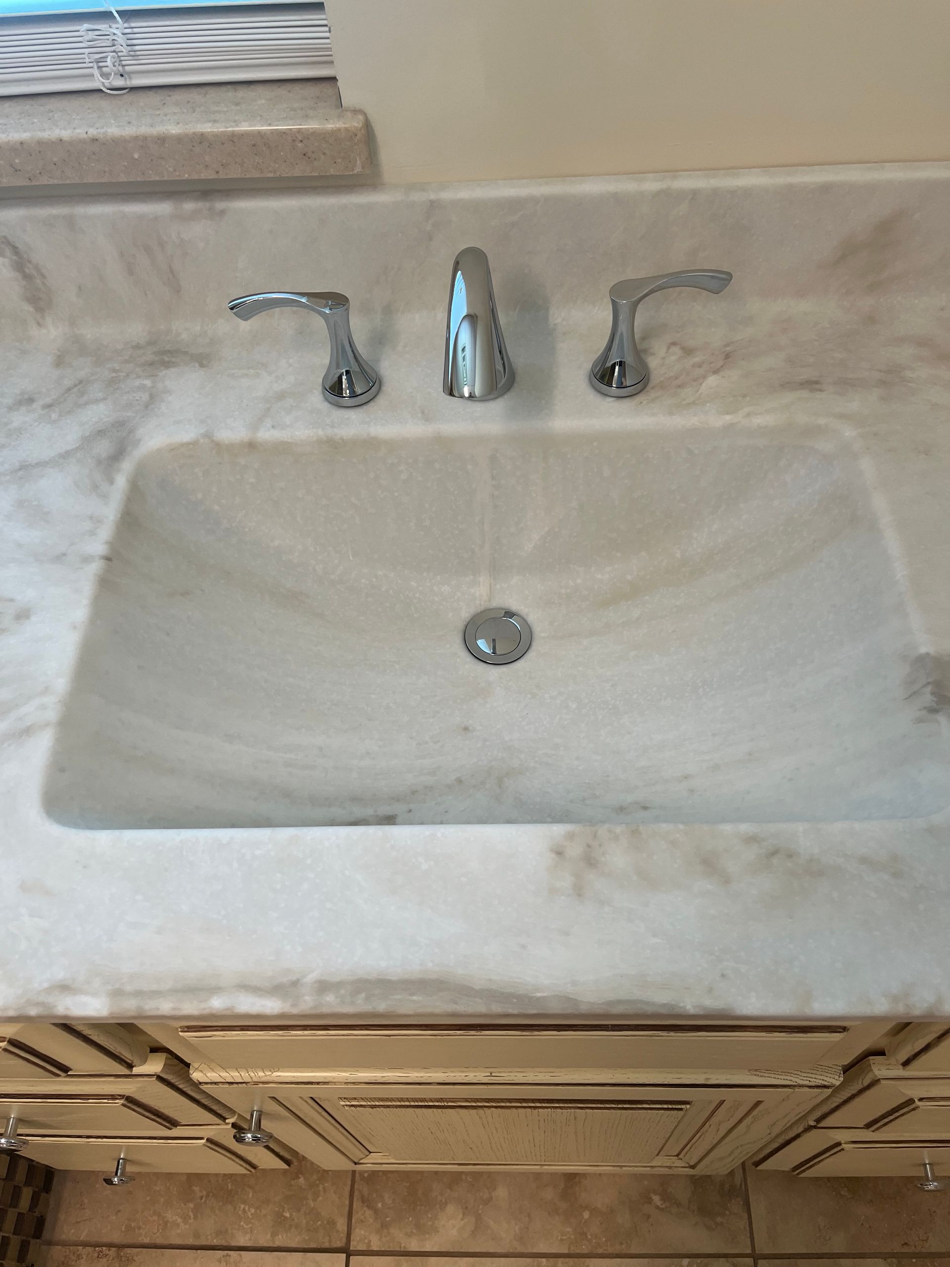 Bathroom sink with chrome faucet and handles, white marble countertop, and cabinet below