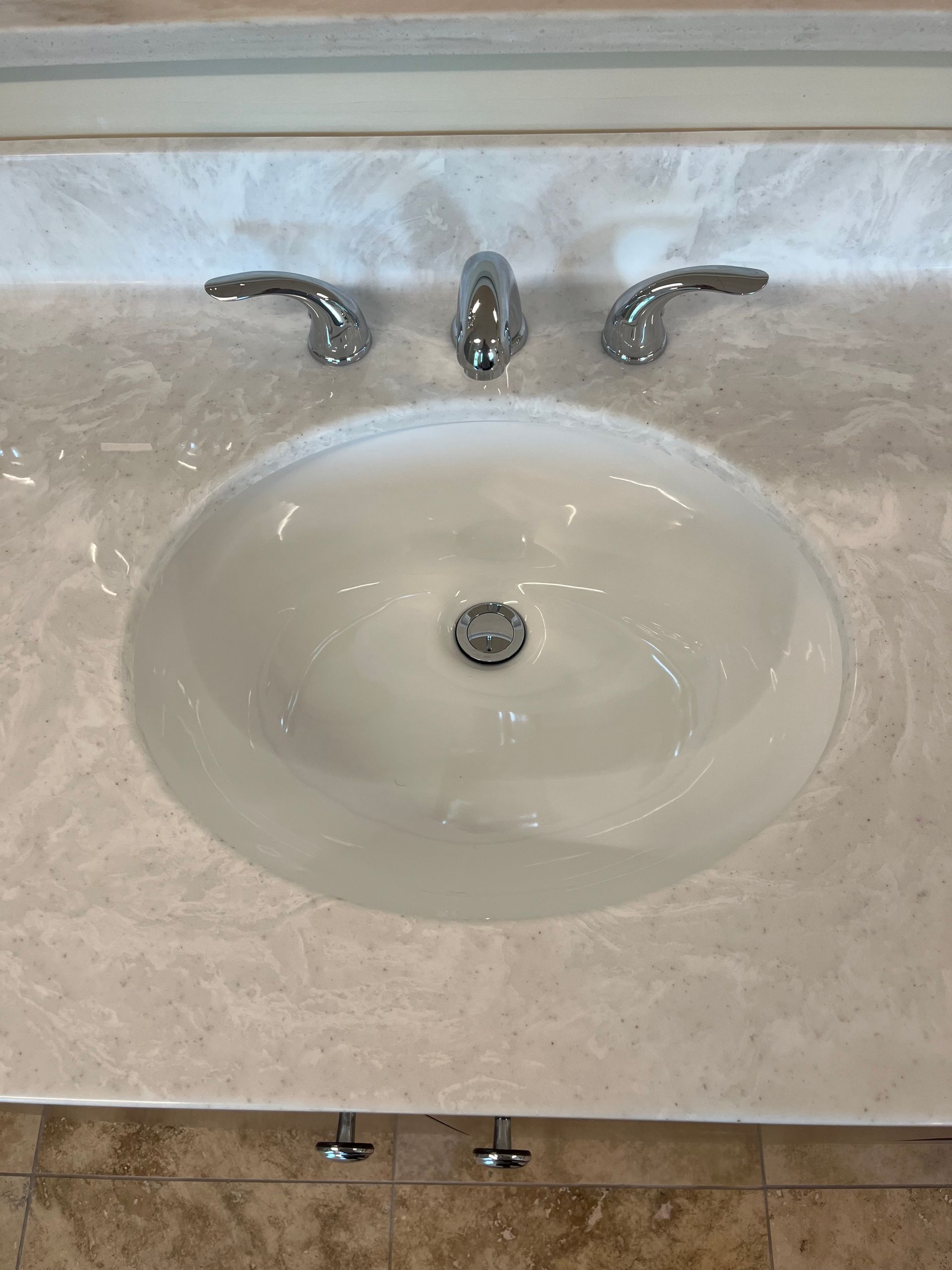 Bathroom sink with beige countertop and chrome faucet over an oval white basin.
