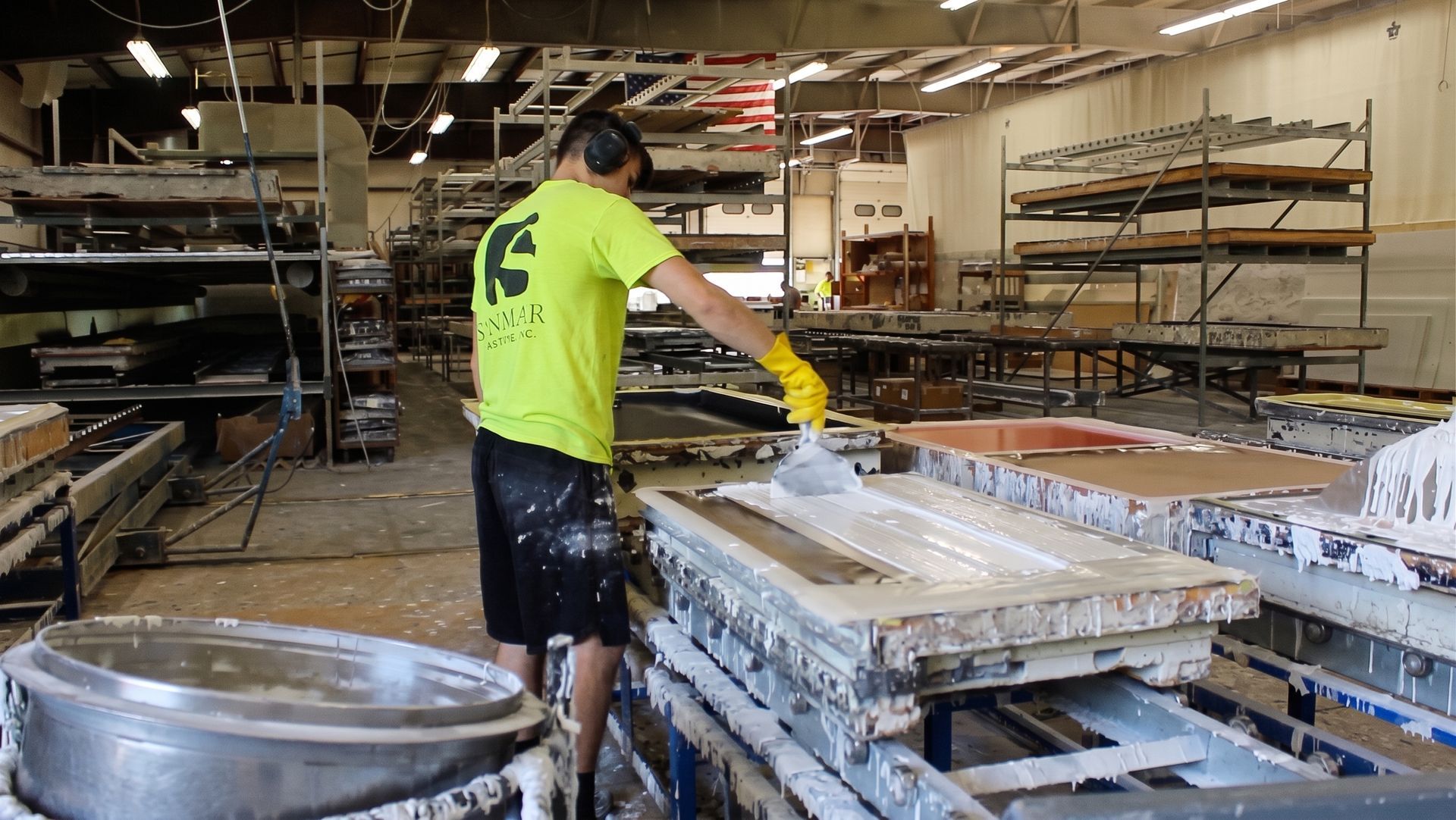 Worker in a neon shirt spreads material on a large mold in an industrial workshop.