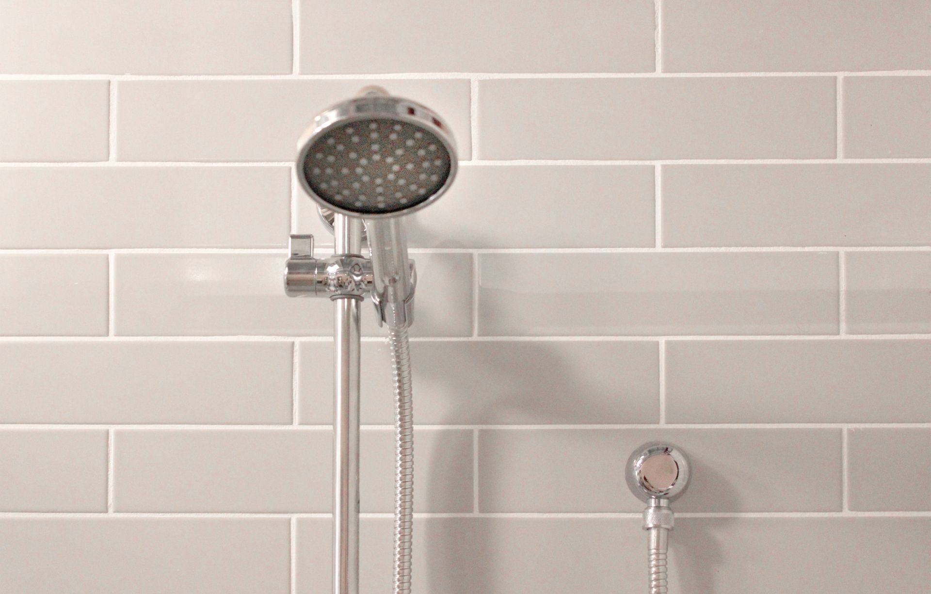 Chrome showerheads on a light tiled bathroom wall
