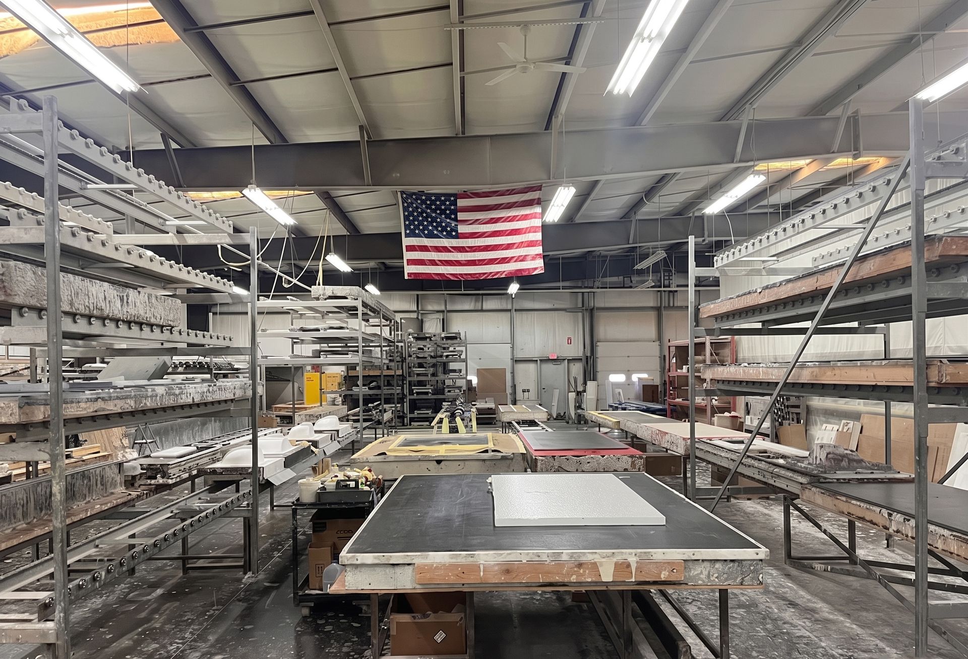 Industrial workshop with metal shelving, worktables, and a large American flag on the back wall.