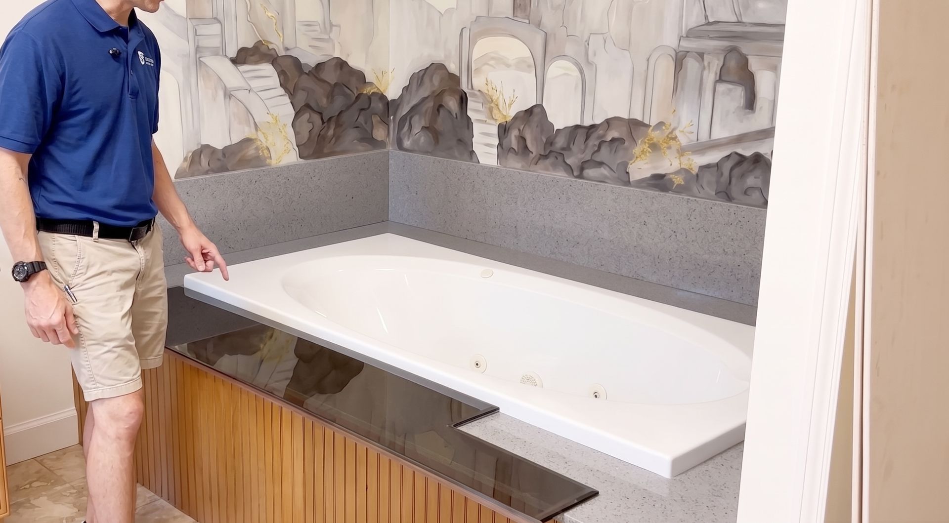 Man standing beside a large white bathtub in a showroom with stone wall decor