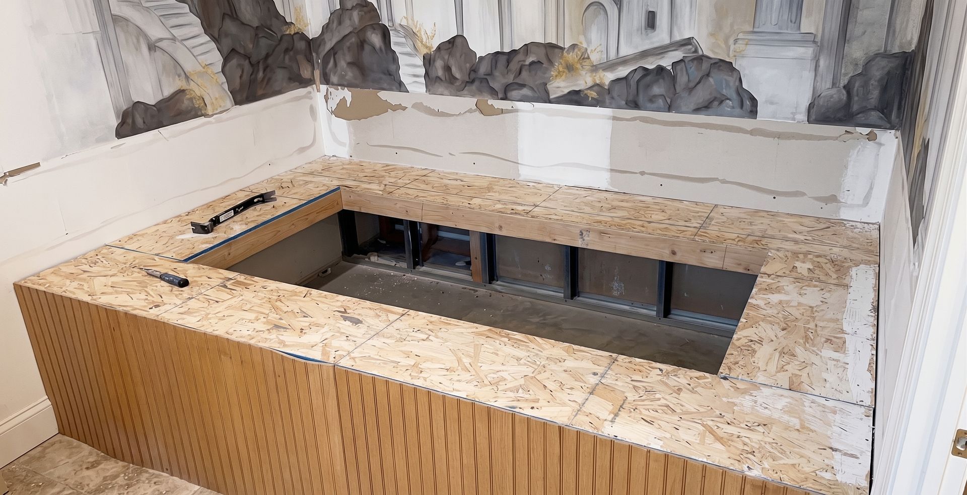 Rectangular built-in bench with a speckled stone top and black interior opening beneath a mural wall.