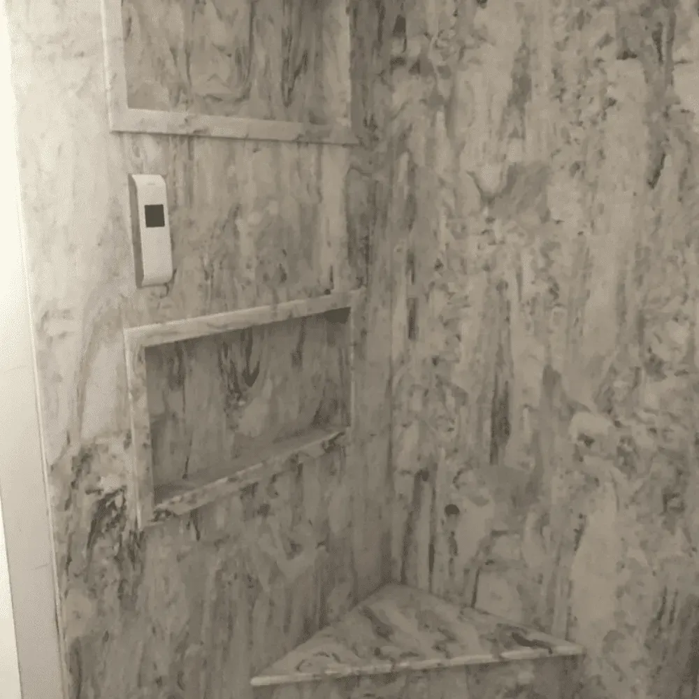 Marble-patterned tiled shower corner with built-in shelves and a wall control panel