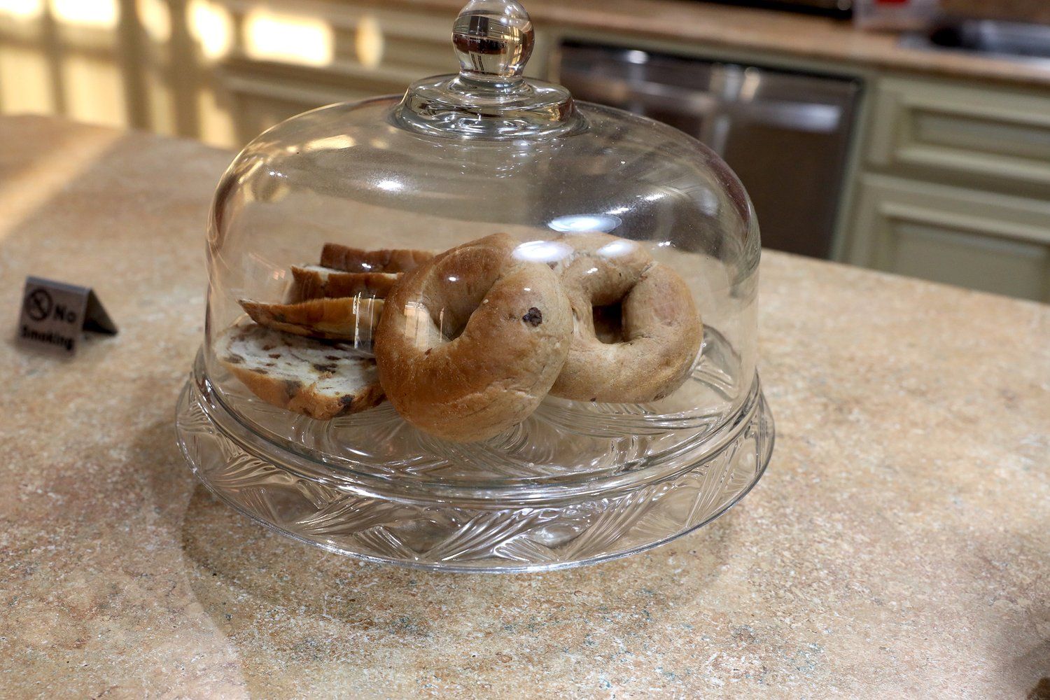 Three bagels are sitting under a glass dome on a counter.