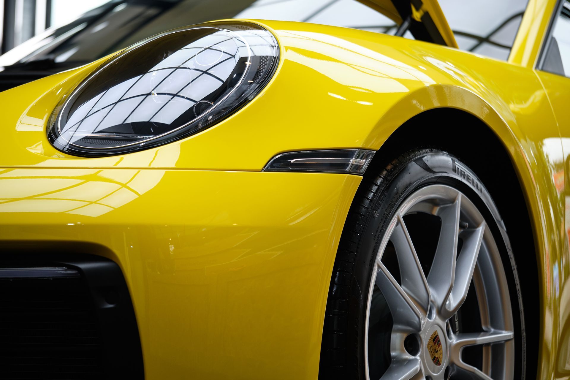 Yellow sports car close-up showing front wheel and headlight in a showroom