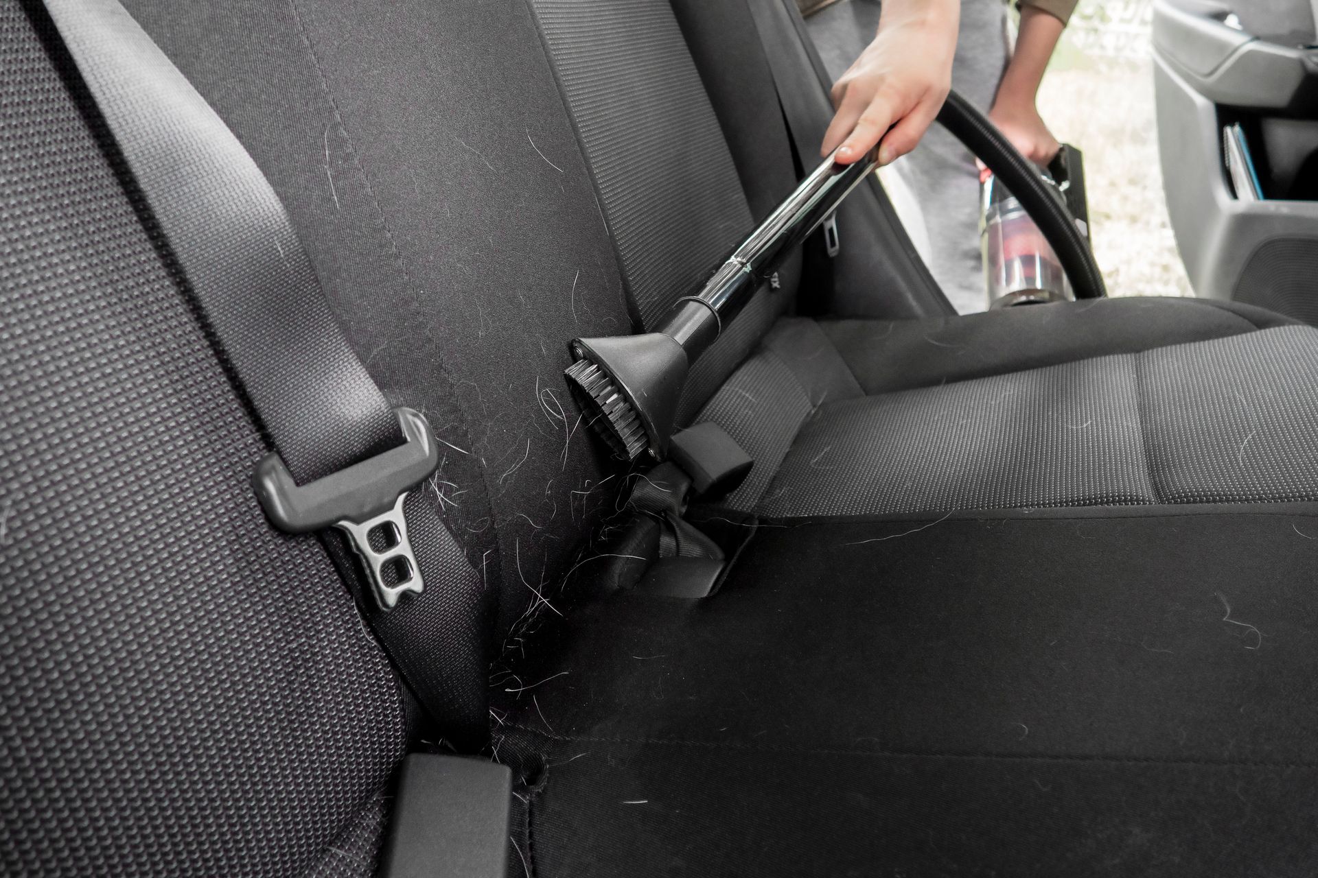 Person vacuuming the back seat of a car with a handheld vacuum cleaner