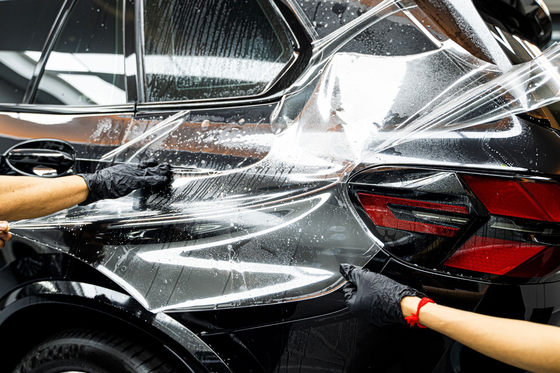 Two people washing a black car with soapy water and spray
