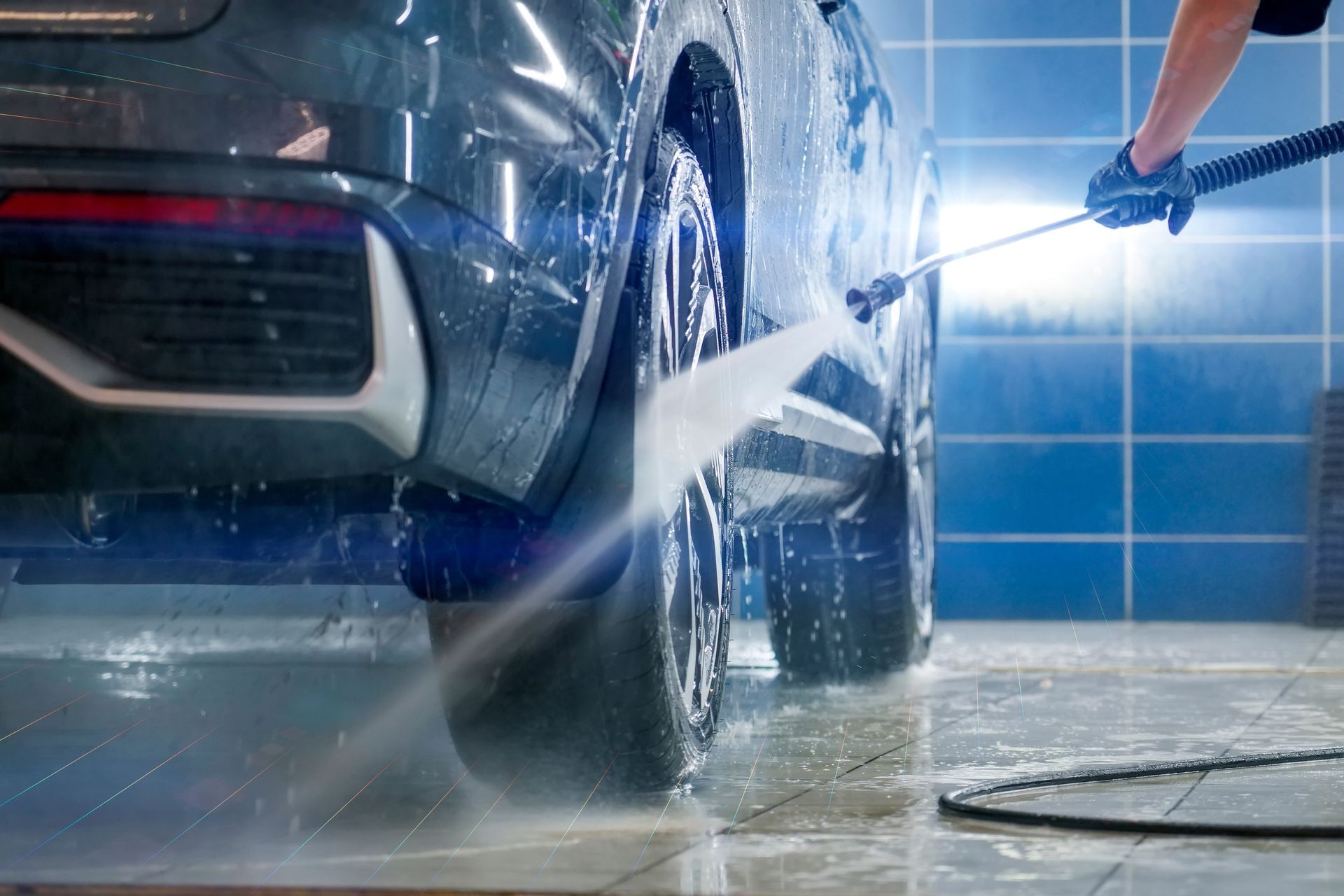 Person pressure-washing a blue car in a wet garage area