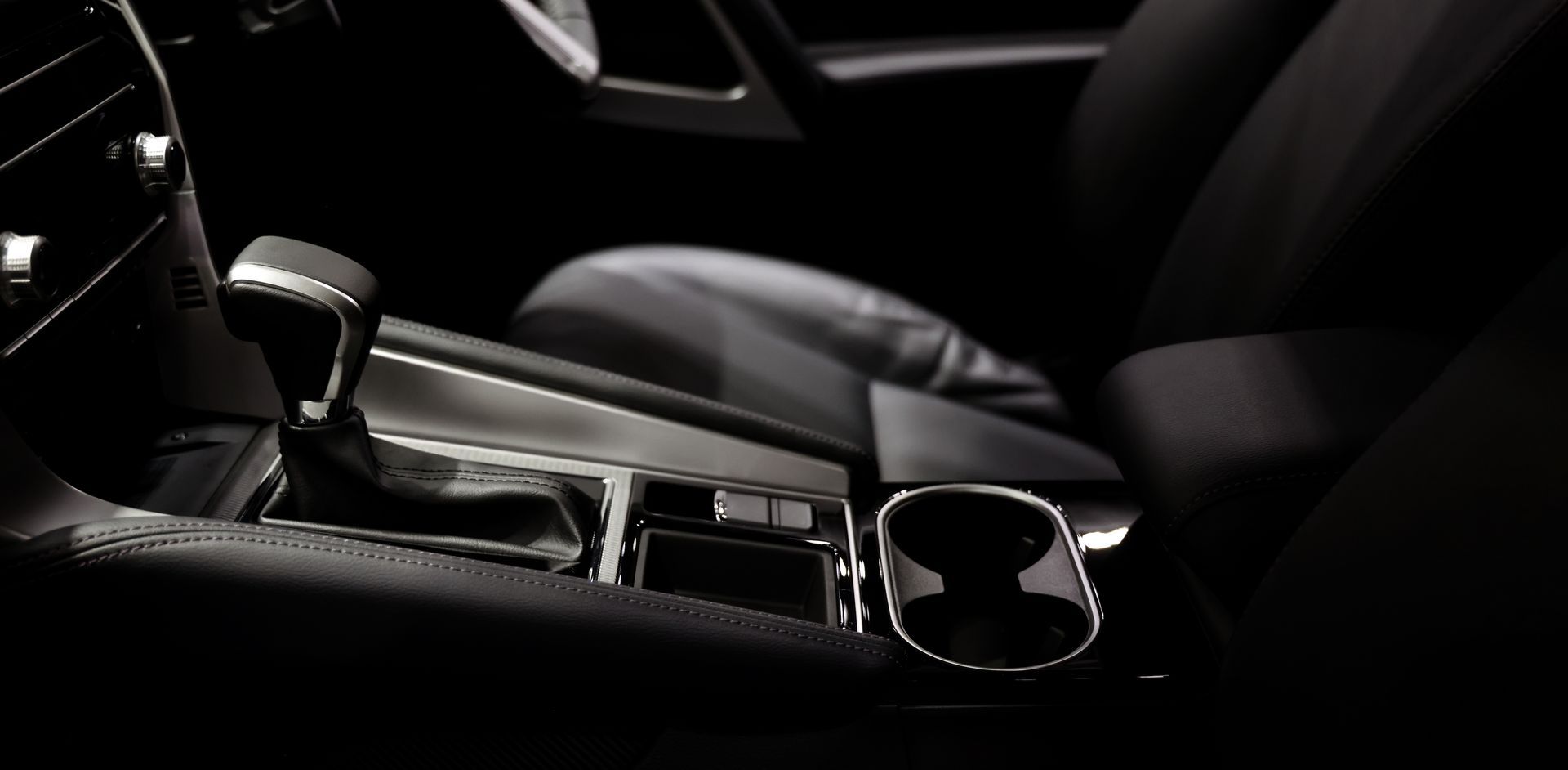 Car interior with black center console, gear shifter, cup holders, and front seat in low light