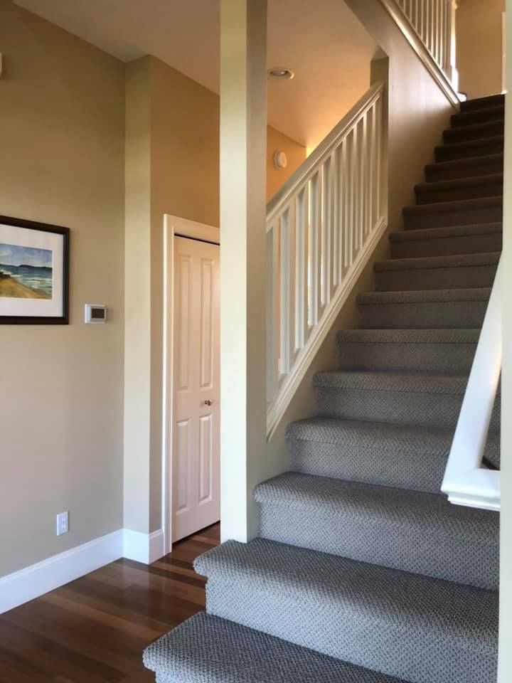 Interior hallway with staircase, closet, and artwork; beige walls and light wood floors.