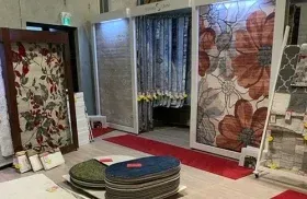 Showroom display of patterned curtains and blinds in a home decor store, with sample rugs on the floor