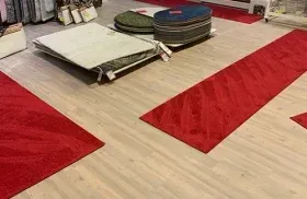 Red carpet runners on a light wood floor with low display tables and stacked cushions in a room