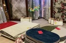 Displayed carpets and rugs in a showroom, including white, blue, and patterned options with price tags