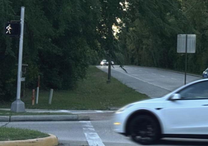 Vehicle turning left across crosswalk with lit crossing sign