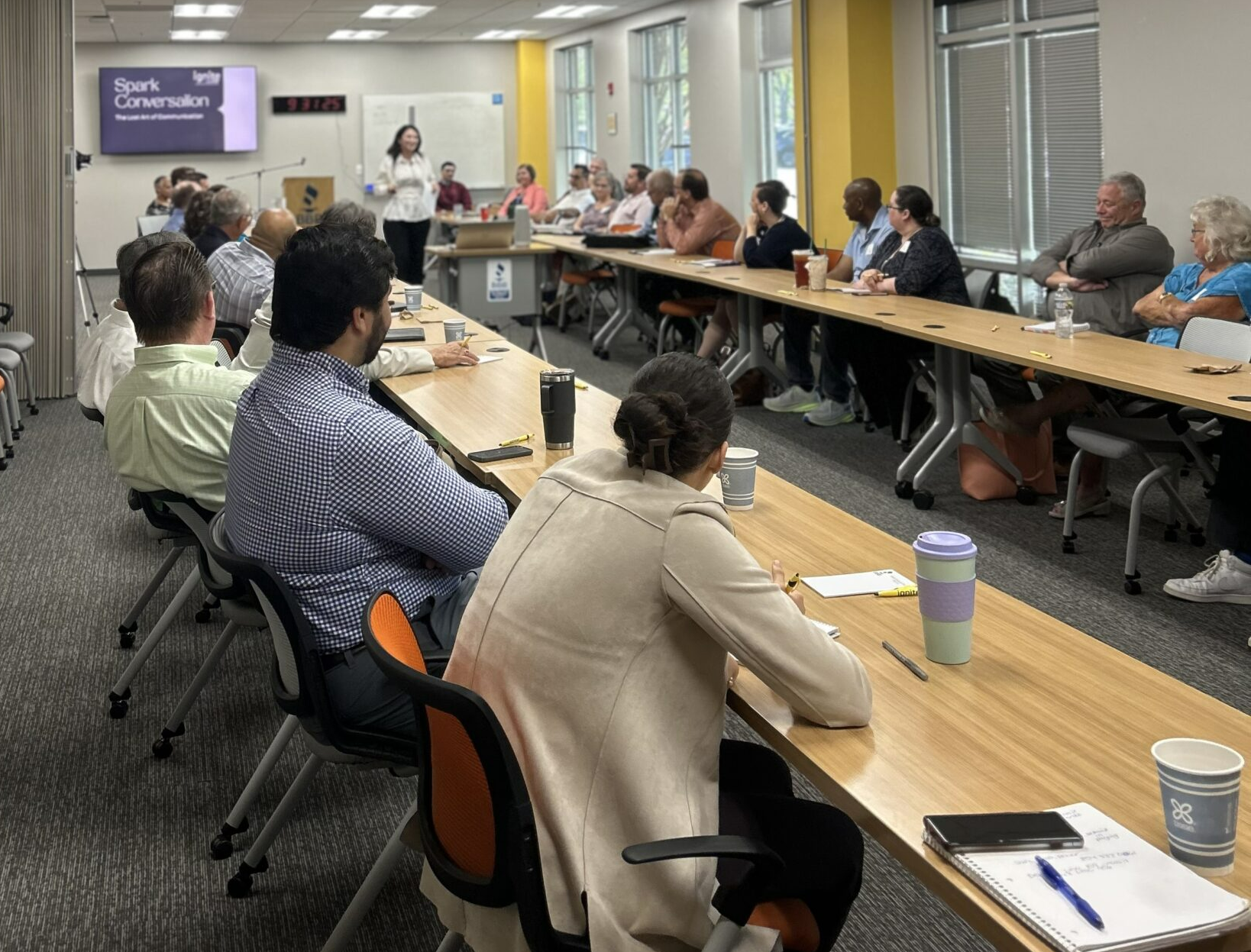 Group of people in a long conference table listening to a presentation in an office setting.