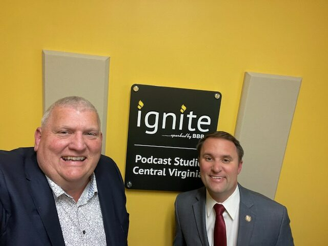 Two men smiling in a podcast studio in front of a sign that says