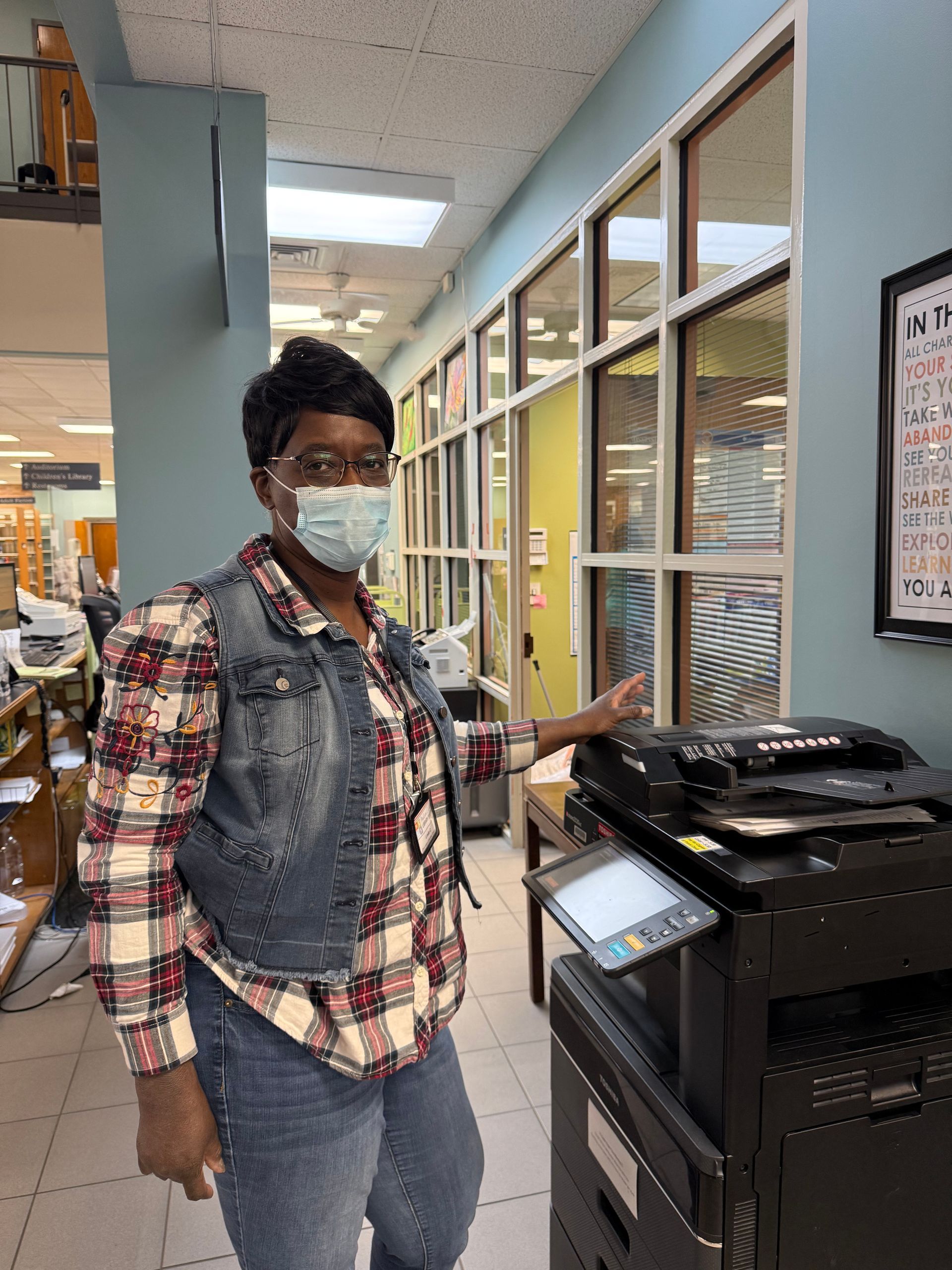 Person wearing a mask stands in a store aisle beside a printer/copier.