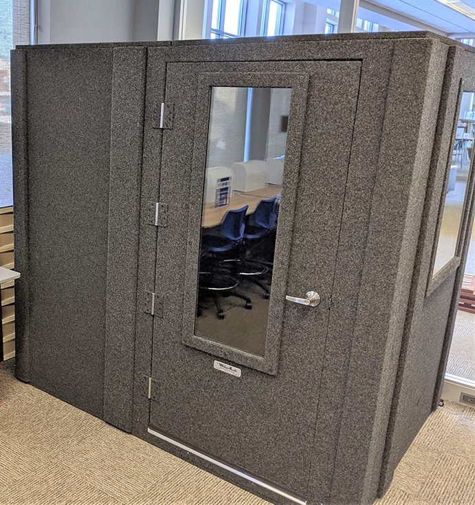 Gray carpeted phone booth with a door window and dark interior in an office setting