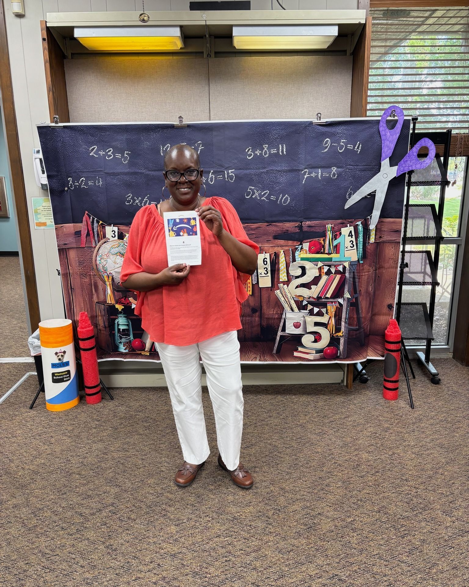 Person in red shirt holding a book in front of a chalkboard-style display with purple ribbon decor.