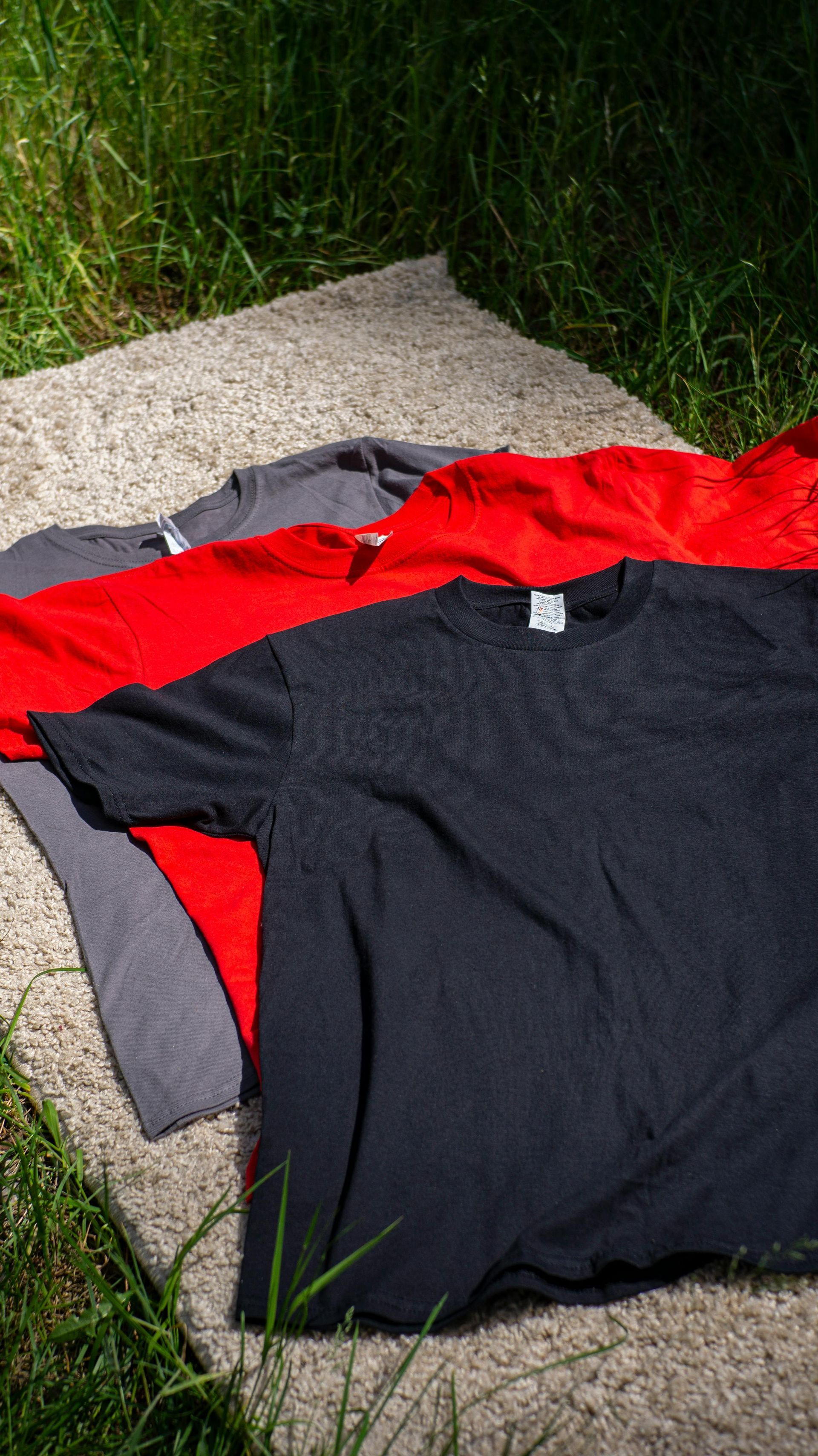 Red, gray, and black shirts laid out on a concrete path beside grass.