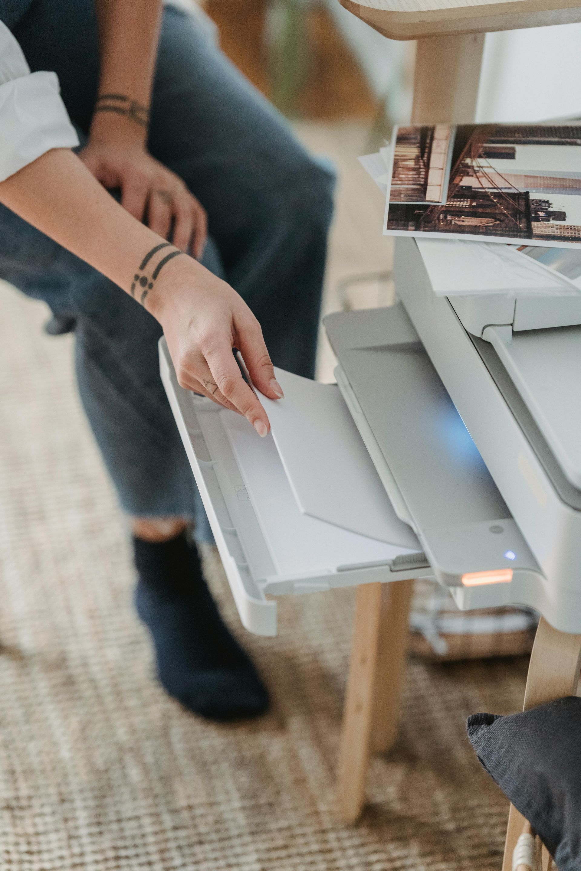 Person loading paper into a printer beside a laptop on a wooden desk
