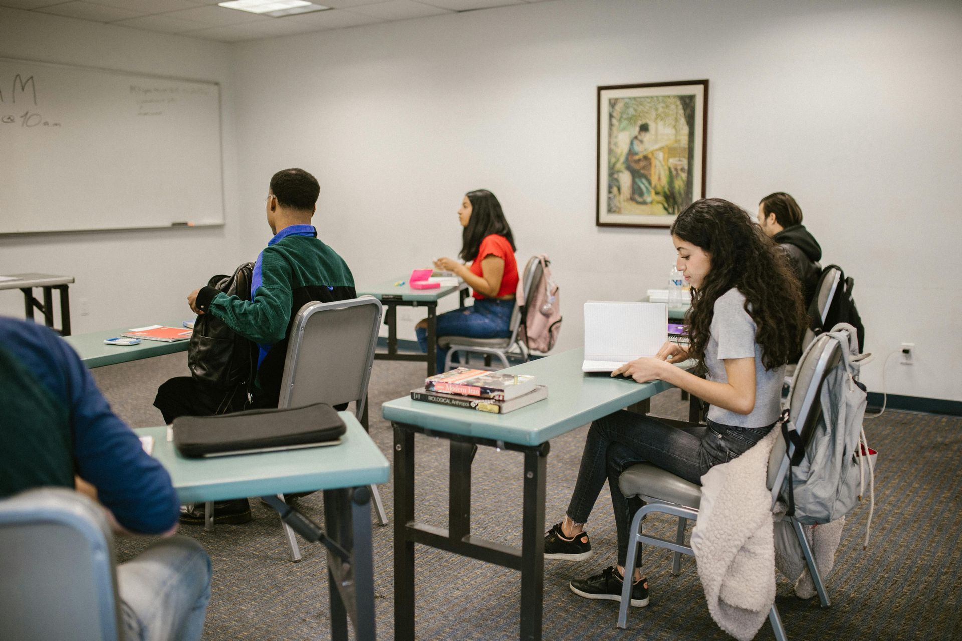 Students seated at desks in a classroom, writing and using laptops during class