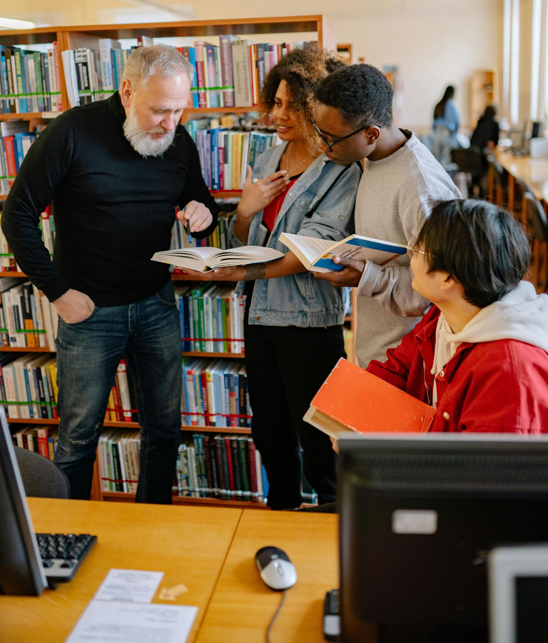 People gathered in a library, discussing books near a shelf-lined reading area.