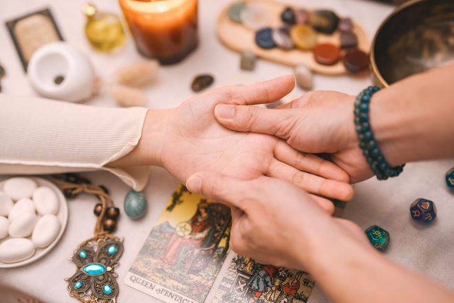 Hands stacked in a healing session with crystals, candles, and tarot cards on a table