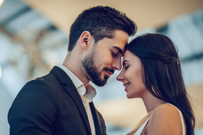 Couple leaning forehead to forehead, eyes closed, in a softly blurred outdoor setting