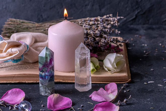 Pink candle with crystals, flowers, and rose petals on a dark tabletop