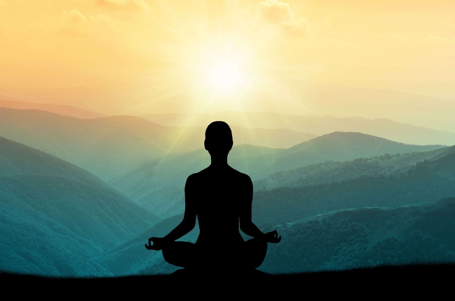 Silhouette of a person meditating on a hill at sunrise above layered mountains