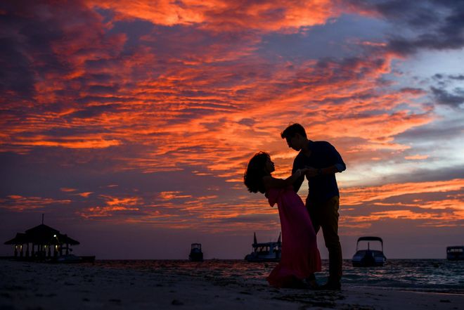 Silhouetted couple dancing on a beach at sunset under dramatic orange and purple clouds