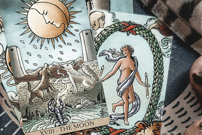 Two tarot cards on a patterned cloth, showing a moon over two animals and a nude figure in a wreath.