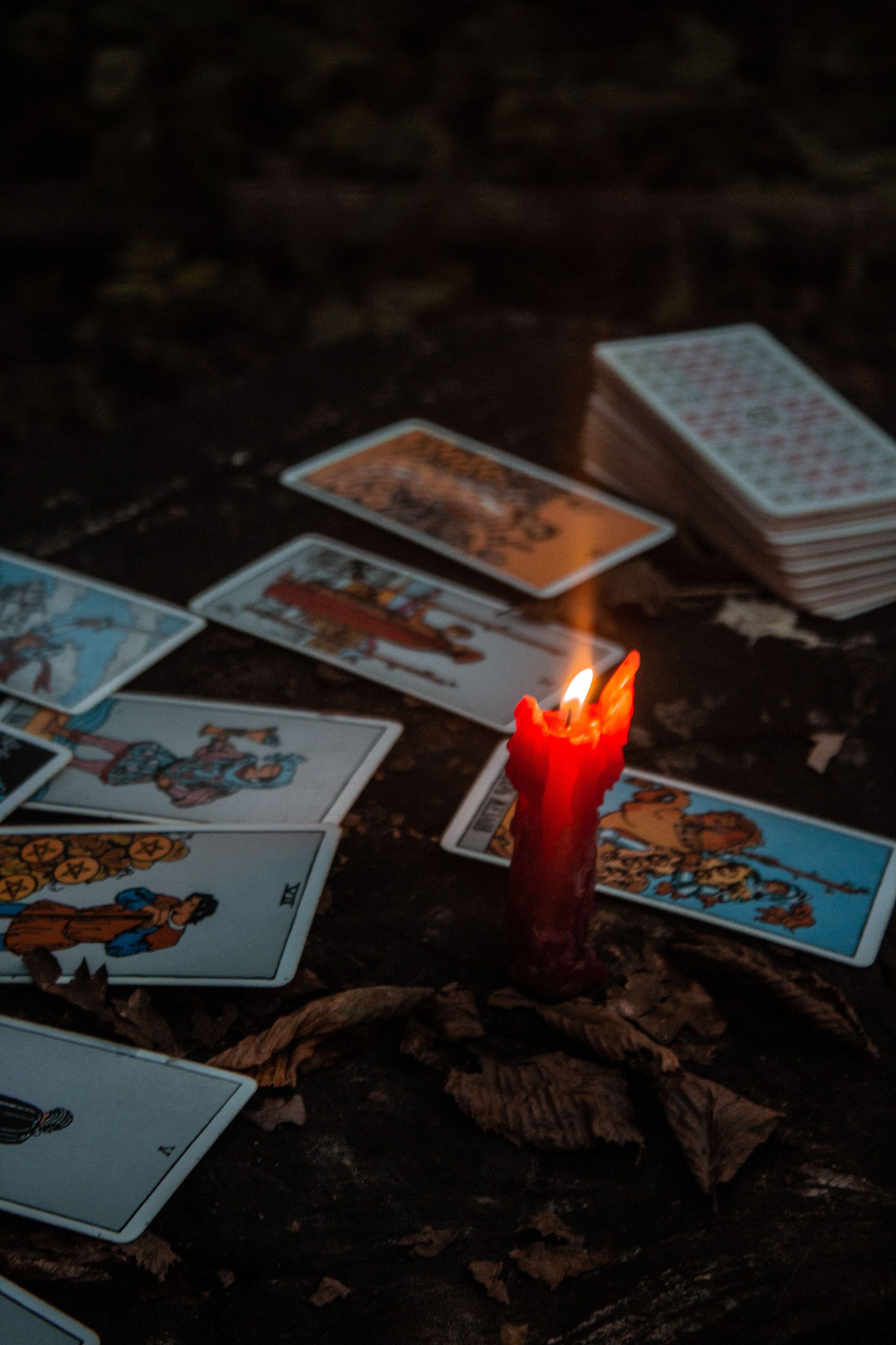 Tarot cards laid around a lit red candle on a dark surface, with a stacked deck nearby