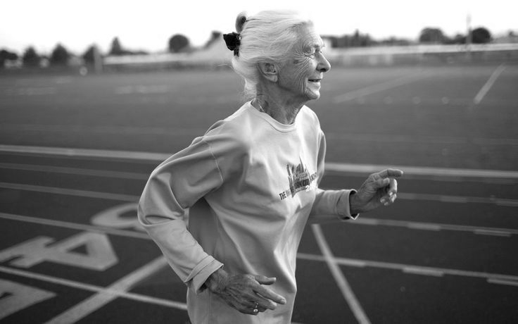 Elderly person running on a track, smiling. Black and white photo.