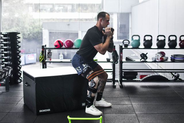 A man is squatting on a box in a gym.