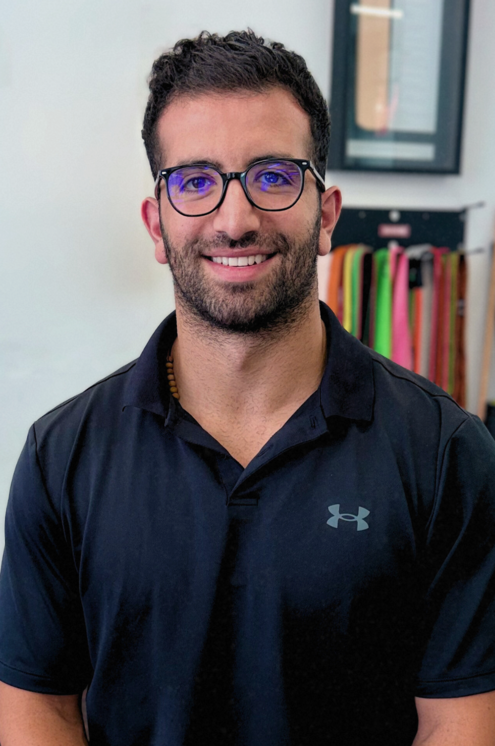 Man with glasses and beard smiles, wearing a black shirt with Under Armour logo.