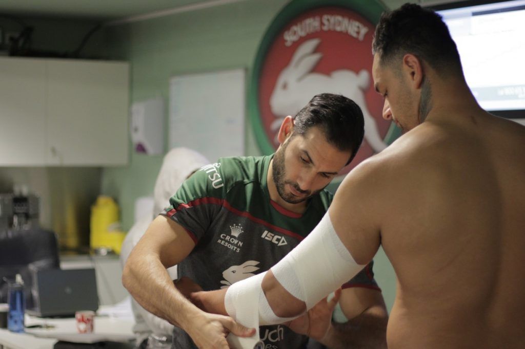 A man with a bandage on his arm is being helped by another man.