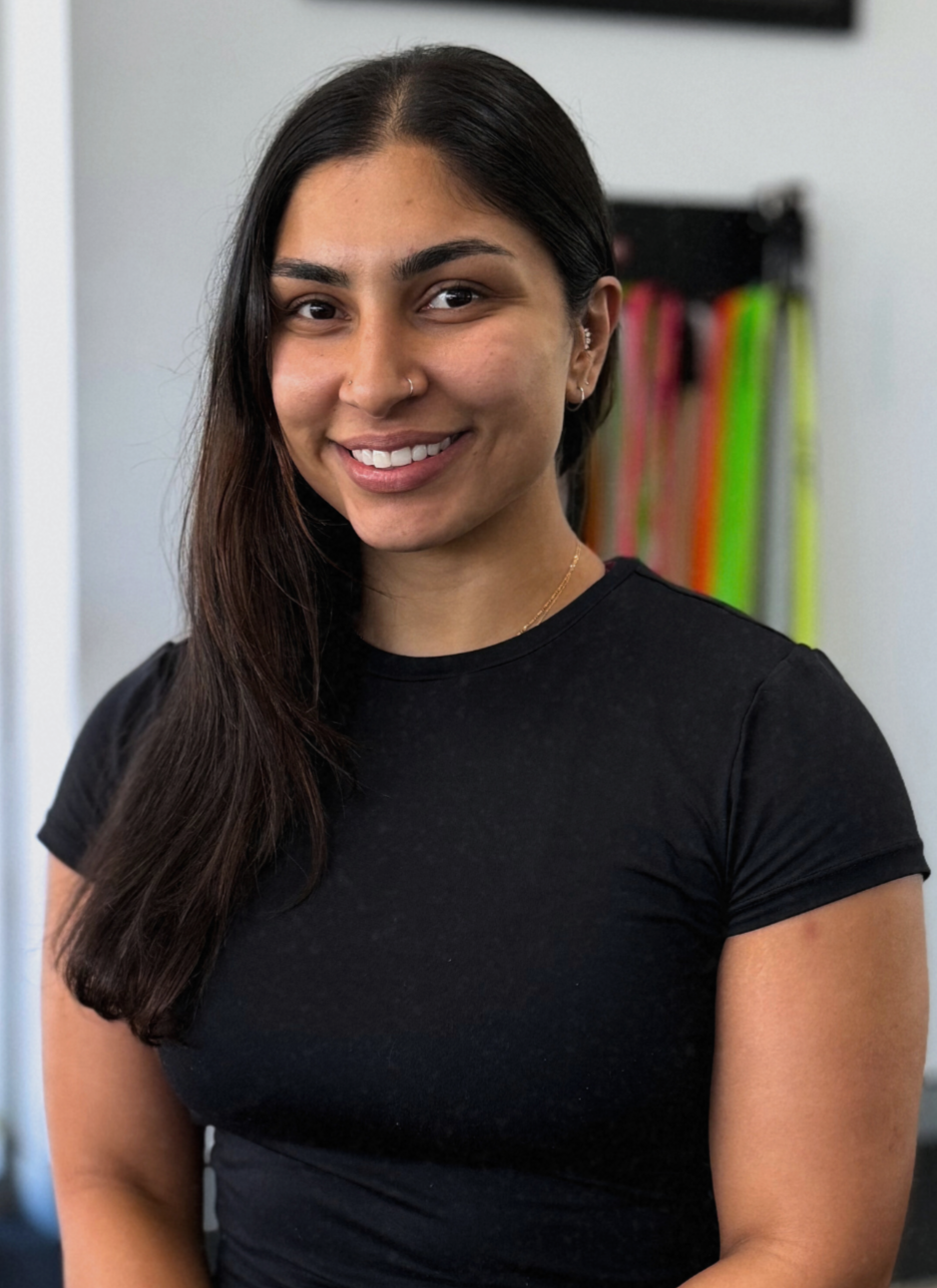 Woman in black shirt smiling, standing indoors, exercise bands in background.