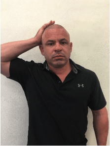 A man in a black under armour shirt holds his hand to his head