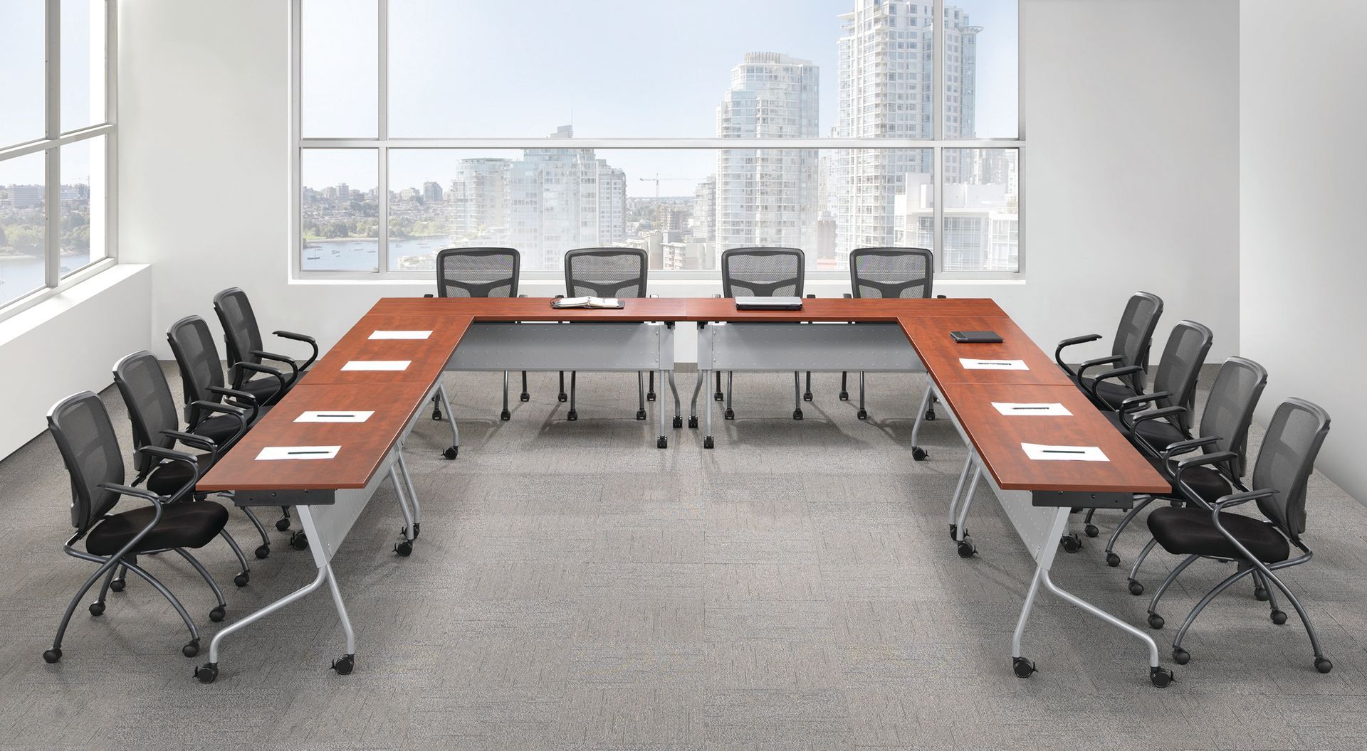 Conference room with u-shaped table, black chairs, and city view through large windows.
