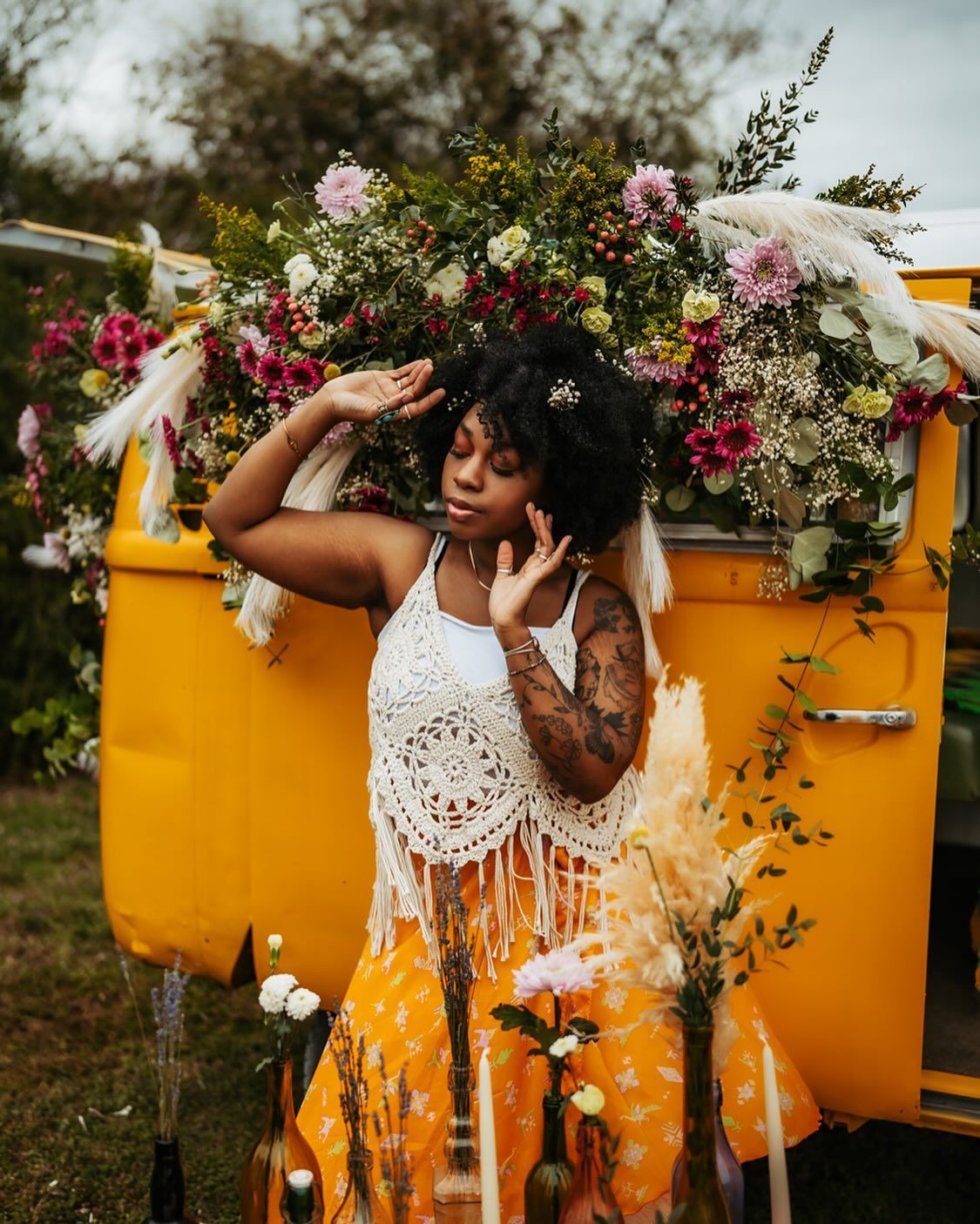 A woman is standing in front of a yellow van covered in flowers.