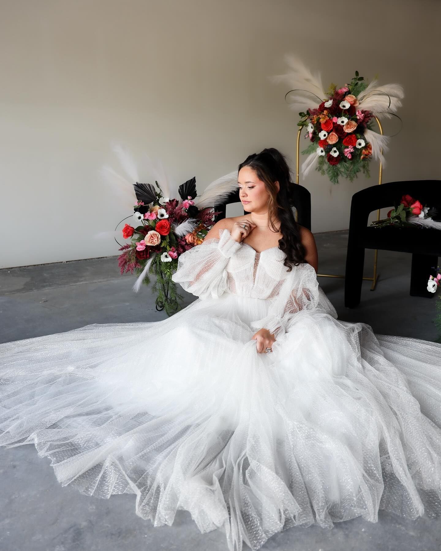 A bride in a white wedding dress is sitting on the floor next to a vase of flowers.