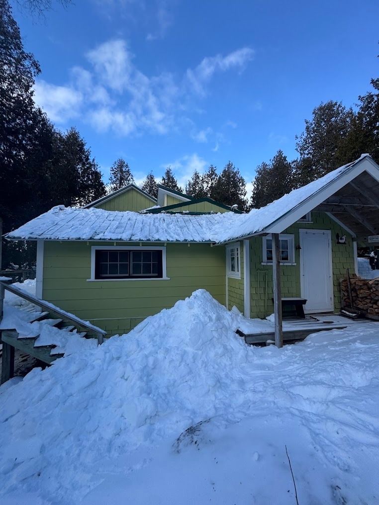 Snow-covered green house with a large snow pile in front under a blue sky
